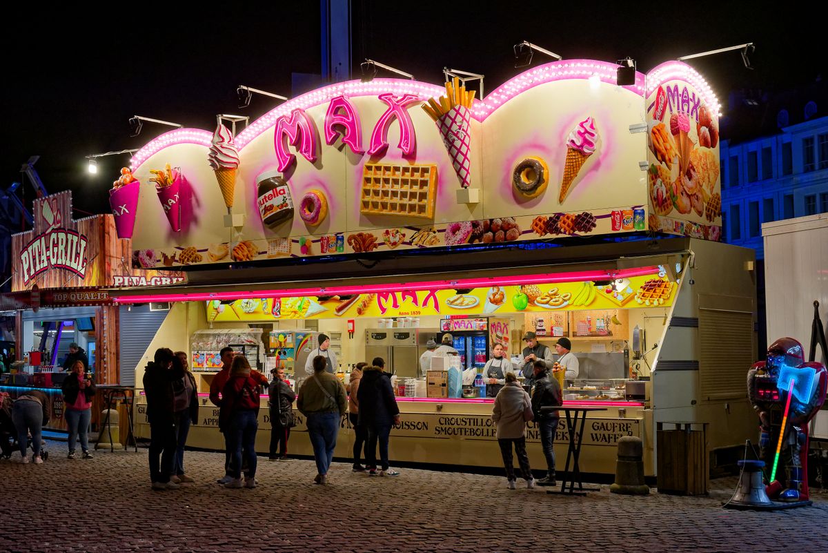 Lit-up street food stand at night with people enjoying sweets and snacks in an urban setting.