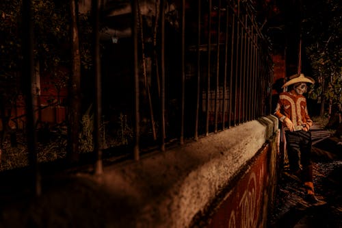 Man in Traditional Clothing and with Painted Face Standing by Fence at Night