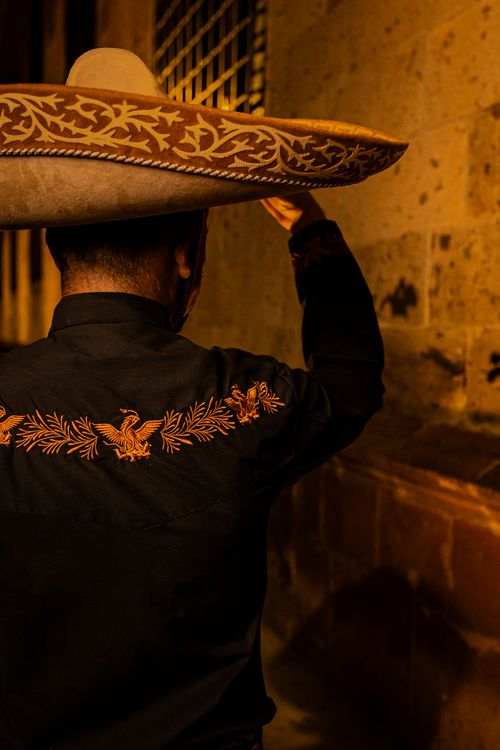 Free Man in traditional Mexican attire with sombrero walking through dimly lit street at night. Stock Photo