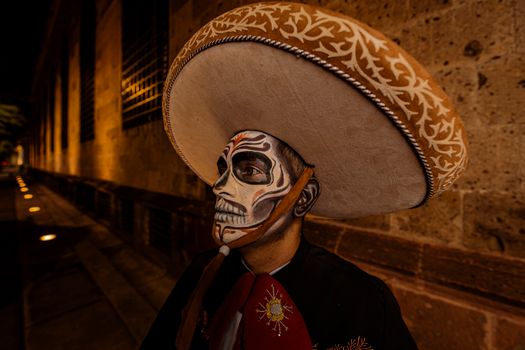 A man in traditional Mexican Day of the Dead makeup and costume at an outdoor festival at night.