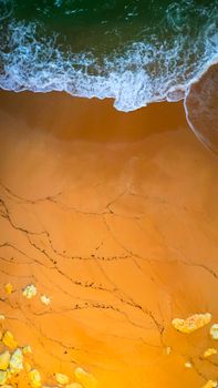 Drone shot of waves meeting a golden sandy beach in Faro, Portugal.