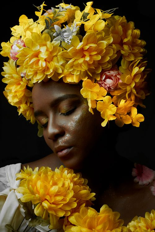 Free Stunning portrait of a woman wearing a vibrant wreath of yellow and pink flowers against a dark background. Stock Photo