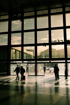 Travelers silhouetted against large airport terminal windows, capturing a moment of travel.