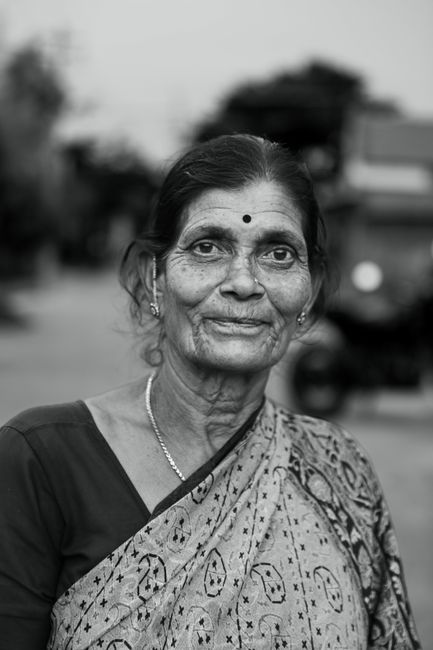 Black and white portrait of an elderly Indian woman standing outdoors in traditional clothing.