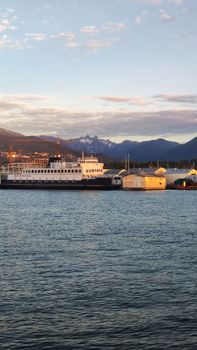 Scenic view of a ferry moored at Vancouver harbor with mountain backdrop and sunset sky.