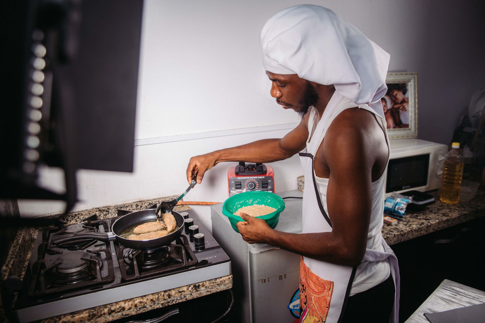 A man in a white hat cooking in a kitchen, focusing intently on his task.