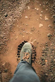 一只靴子踏进室外的泥泞水坑，溅起了土路上的泥水