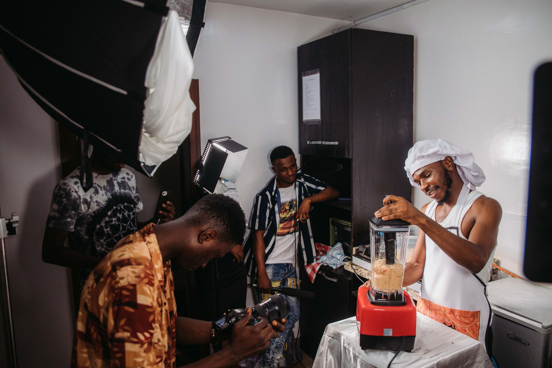 Men recording a cooking scene with a blender in a well-lit kitchen.