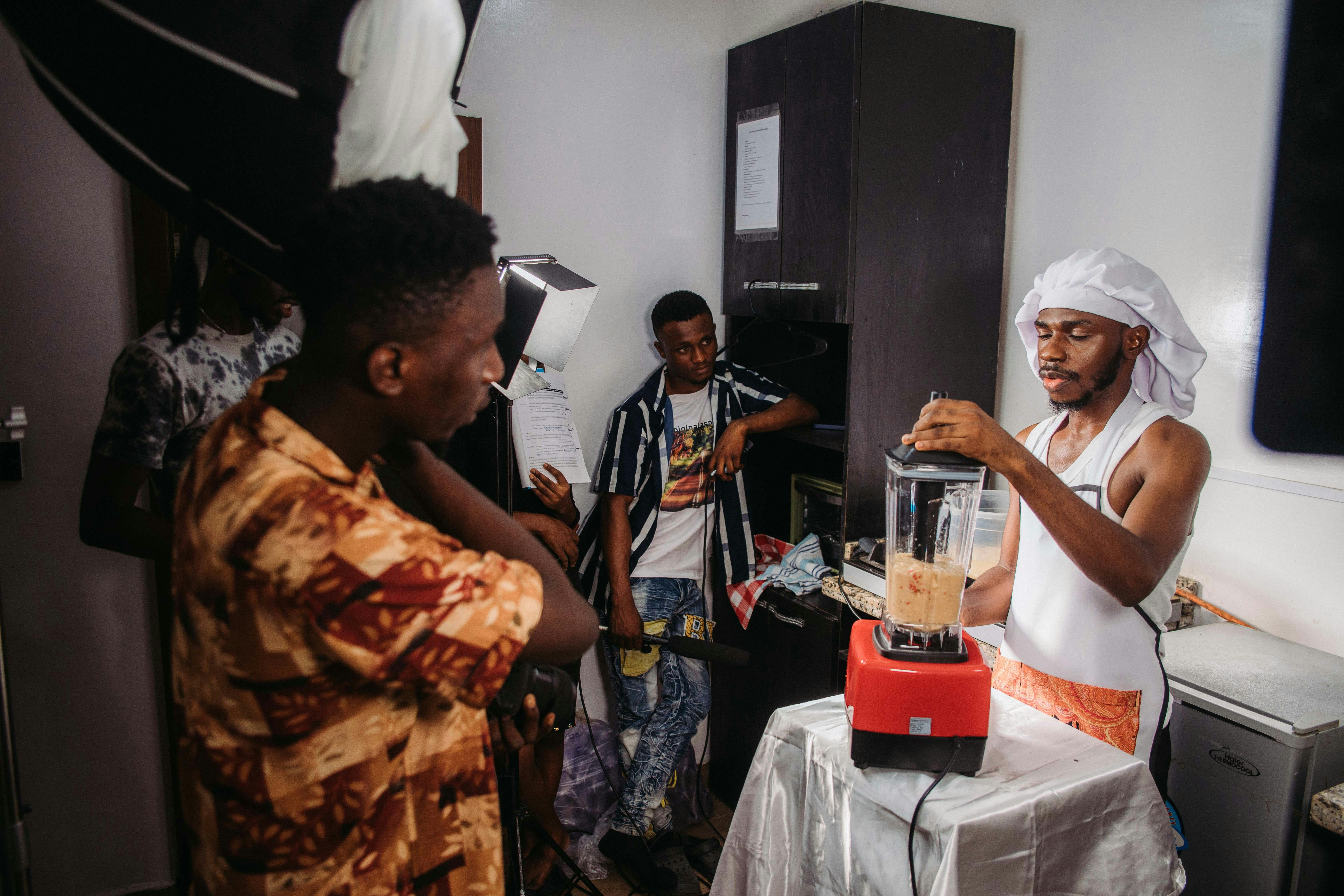 Kitchen filming setup with crew and blender operator during a cooking demonstration.