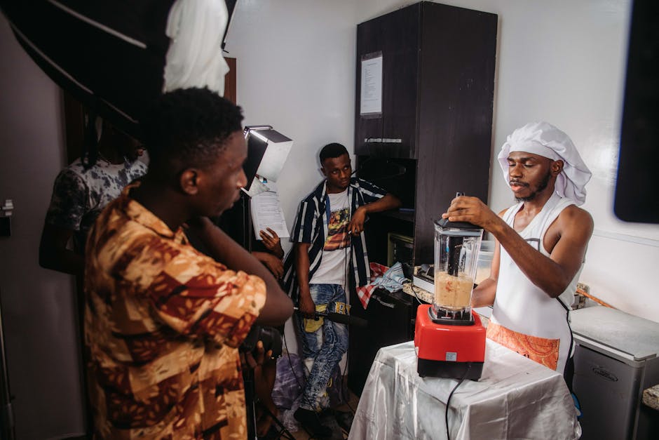 Kitchen filming setup with crew and blender operator during a cooking demonstration.