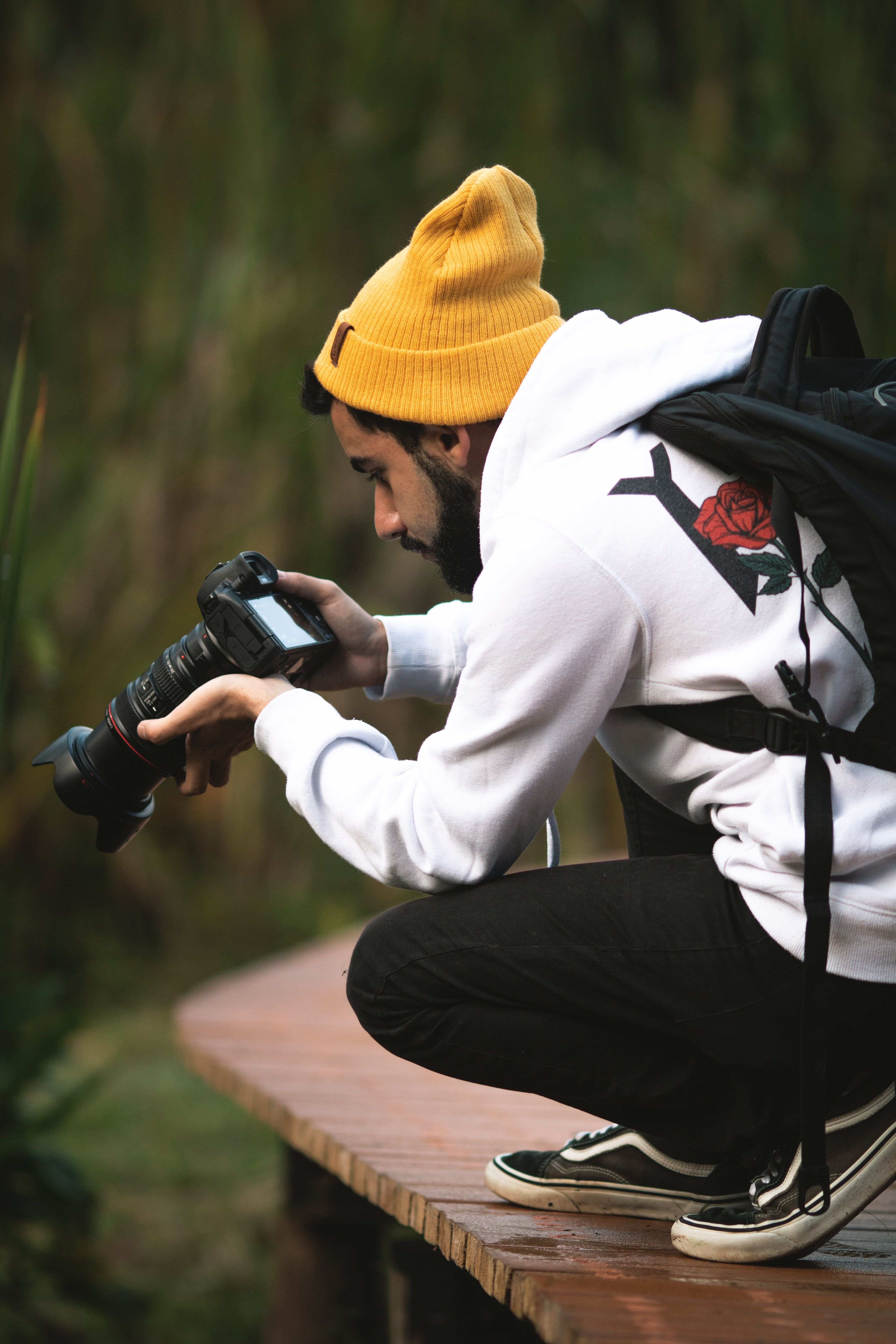 Casual photographer crouching on a wooden path in a park with camera gear.