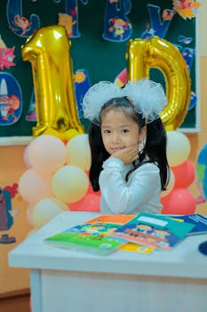 Asian child celebrating her birthday in a decorated classroom with balloons and books.