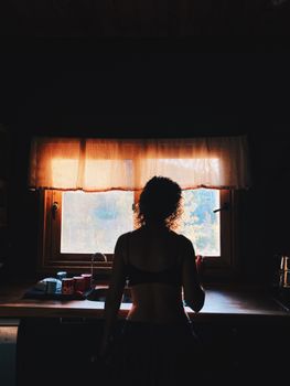 A woman stands in silhouette at a kitchen sink, framed by a softly lit window.