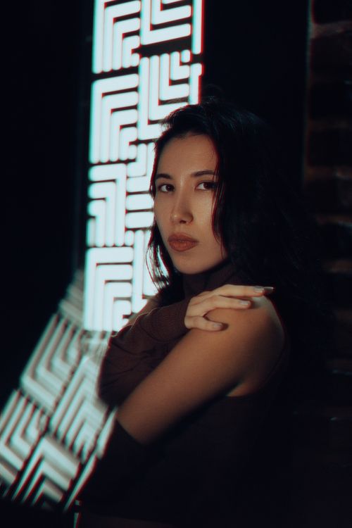 Free A woman poses in front of neon lights, giving a reflective and moody feel. Stock Photo