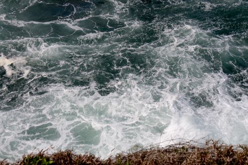 Free Aerial view of powerful ocean waves crashing onto a rocky shoreline with foamy waters. Stock Photo