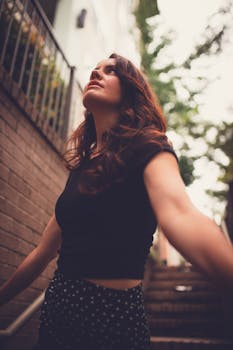 Young woman in a polka dot skirt looking up dreamily in an urban outdoor setting.