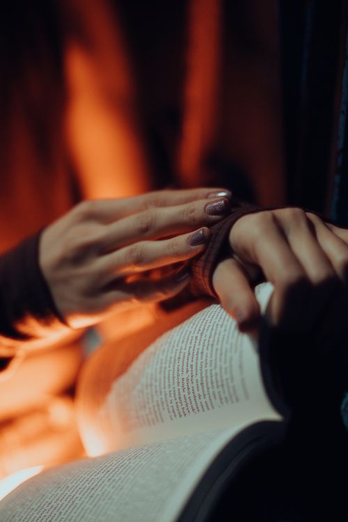 Free Close-up of a woman reading a book in dim lighting, showcasing elegant manicured nails. Stock Photo