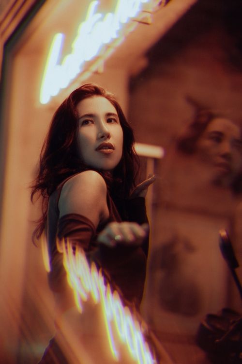 Free Portrait of a young woman posing by neon lights on city streets at night. Stock Photo