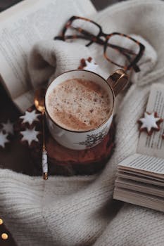 Steaming hot cocoa by an open book, surrounded by cozy warmth and holiday cookies.