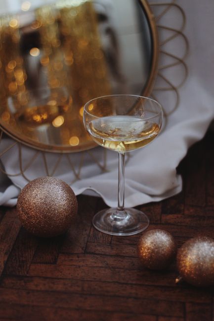 A sophisticated arrangement featuring a wine glass and gold baubles with a mirror reflection.