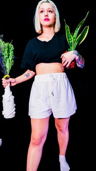 Blonde woman with tattoos holding plants, showcasing style and fashion.