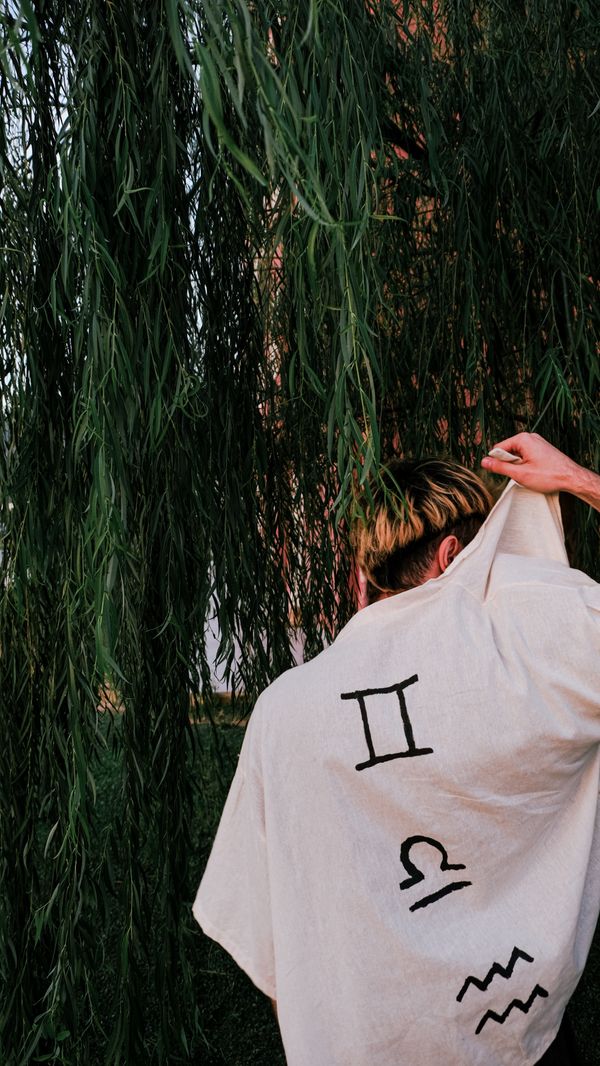Free Person with zodiac symbols on shirt standing under willow tree outdoors. Stock Photo