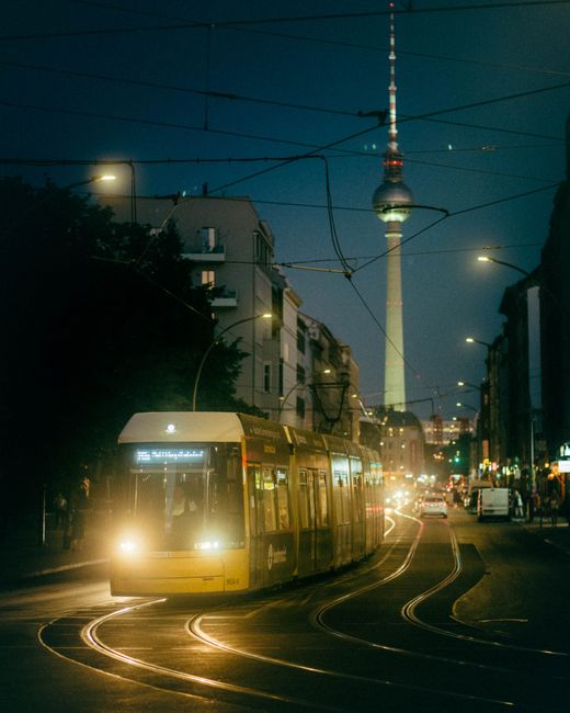 Illuminated Berlin street with tram and Fernsehturm at night.
