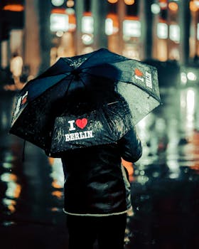 Person holding an umbrella with 'I Love Berlin' in rainy streets at night.
