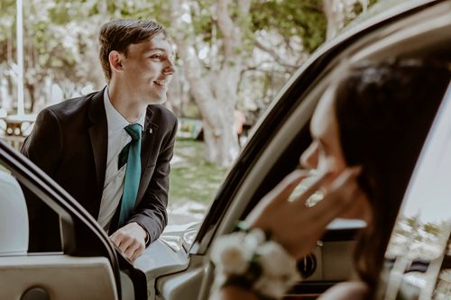 Free A young couple enjoying a sunny day in formal attire, smiling by a car outdoors. Stock Photo
