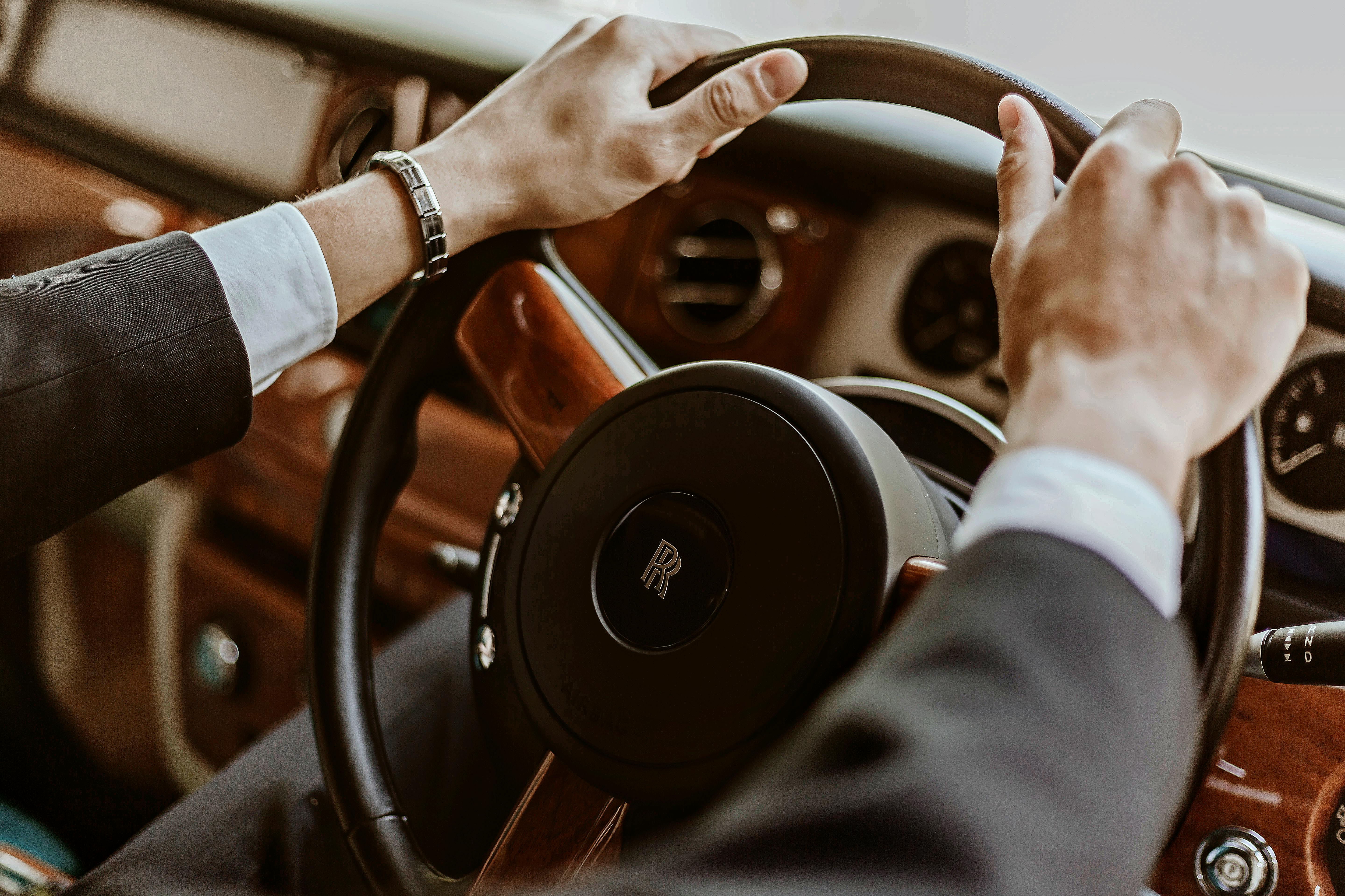 Close-up of man steering vintage Rolls Royce, showcasing luxurious car interior.