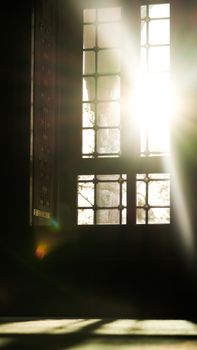 Bright sunlight casts shadows through a grid-patterned window in a dark room.