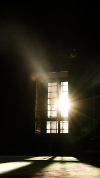 Soft sunlight streams through a vintage window casting shadows in a darkened room.