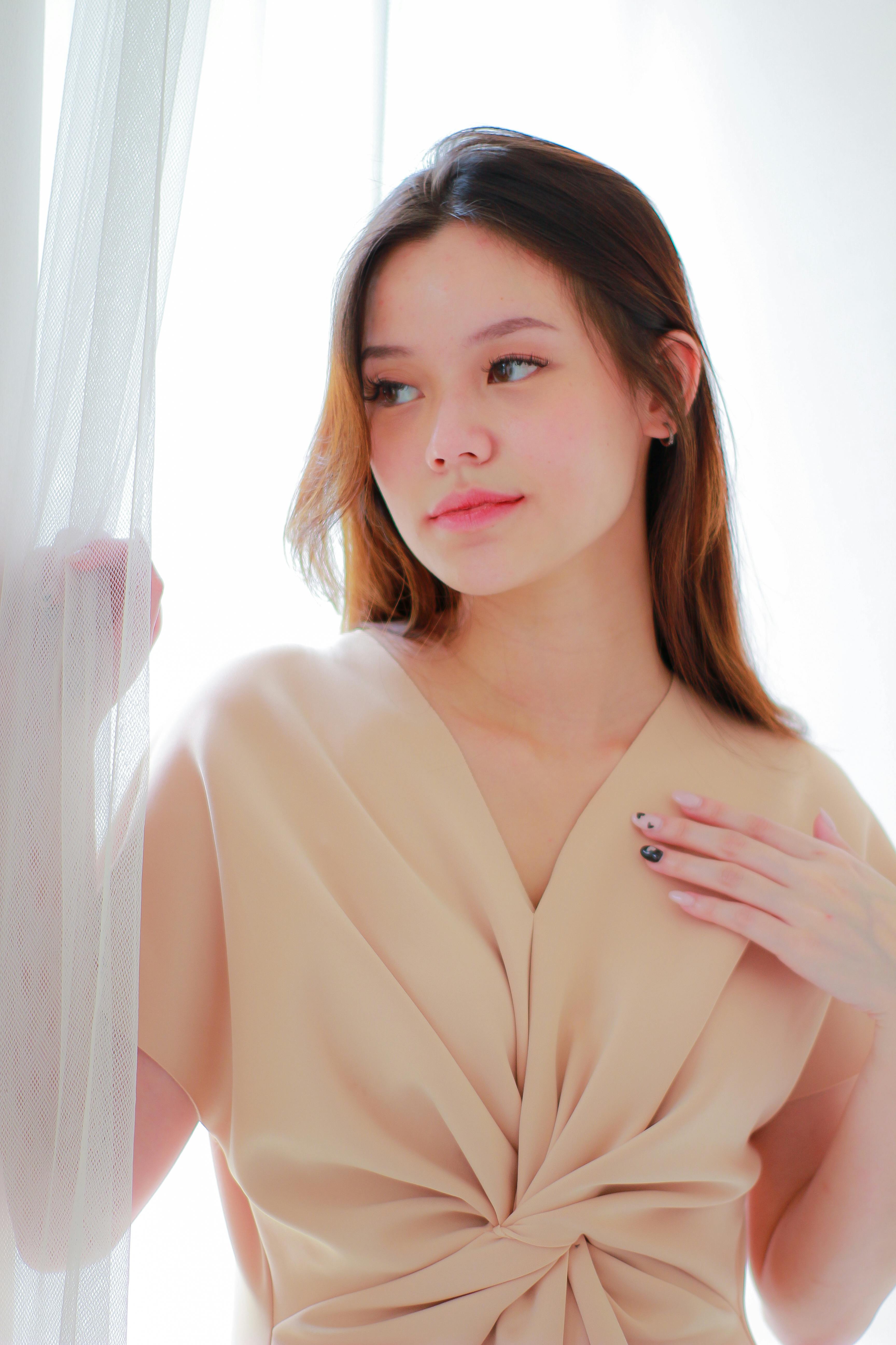 Elegant portrait of a young woman in a beige blouse, softly lit by window light.