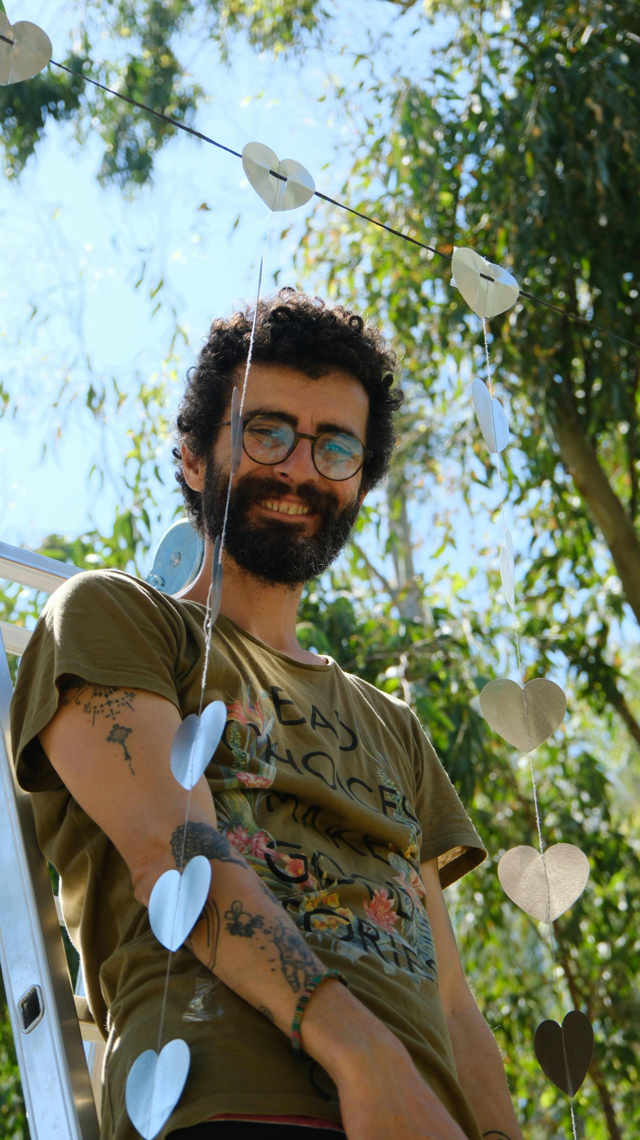 Bearded man with eyeglasses enjoying summer day while hanging heart decorations outdoors.
