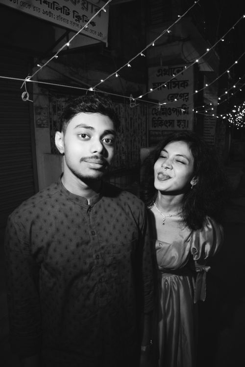 Free A playful black and white portrait of a young couple under festive lights at night. Stock Photo