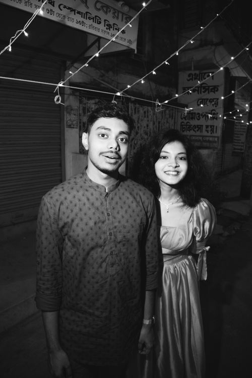 Free A joyful young couple smiles under string lights on an urban street at night. Stock Photo