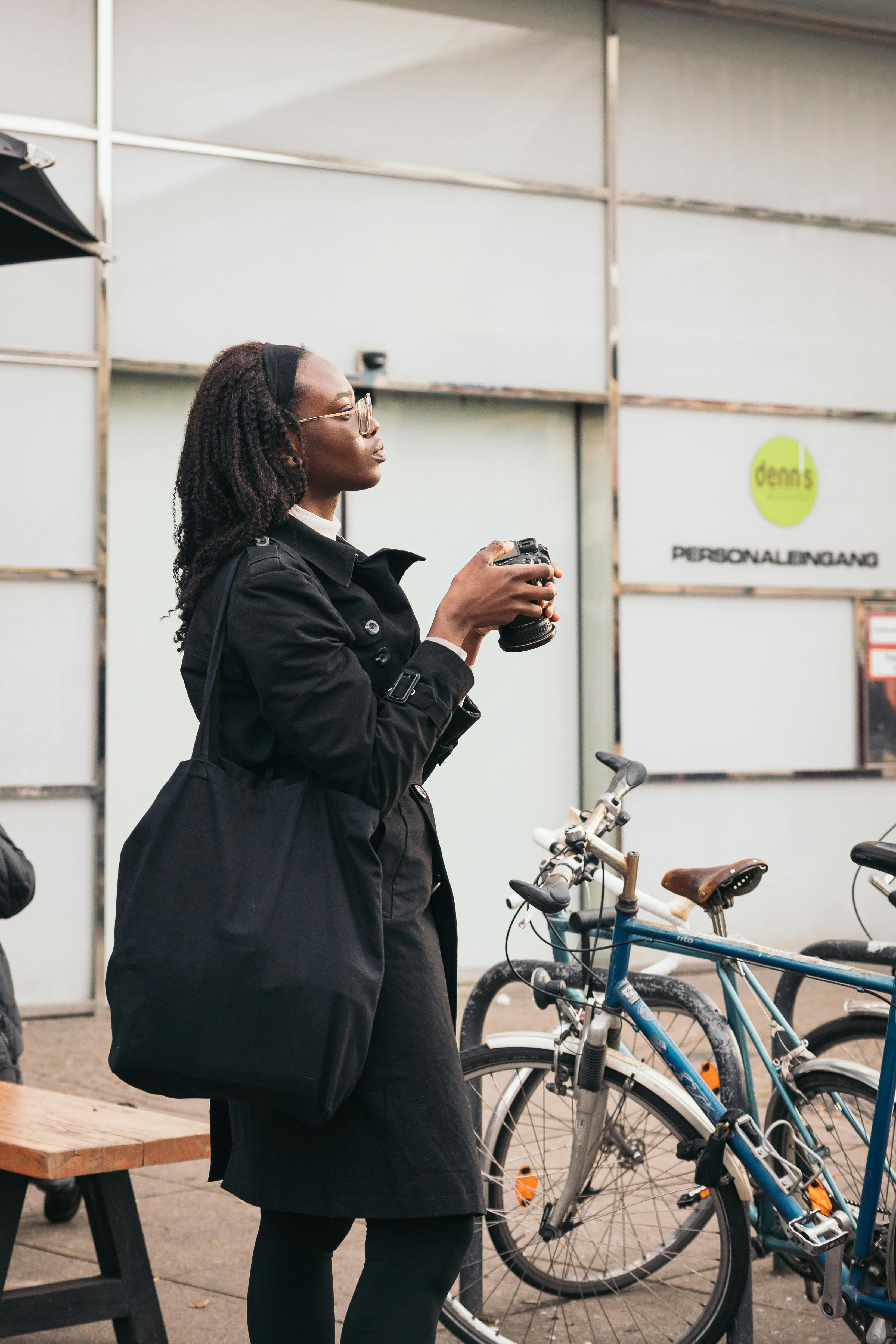 Stylish woman in black coat with camera on a Berlin street near bicycles and modern architecture.