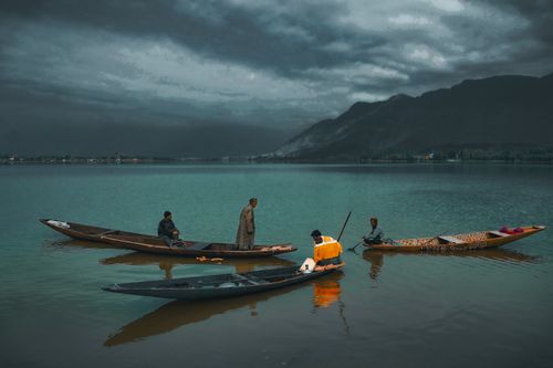 Free Fishermen in wooden boats on Dal Lake, Srinagar, with misty mountains and overcast skies. Stock Photo