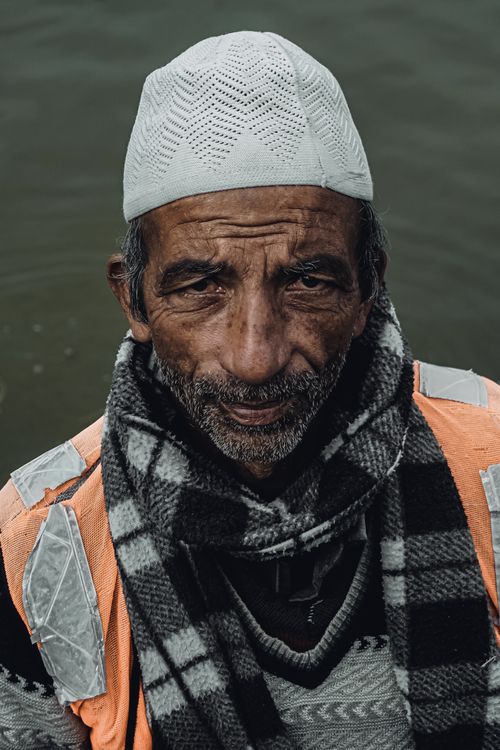 Free Portrait of an elderly man from Srinagar wearing a hat and scarf near water. Stock Photo