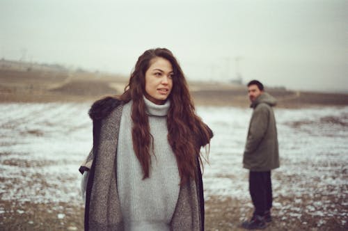 A Man and Woman in Warm Clothes Standing on a Snowy Field 