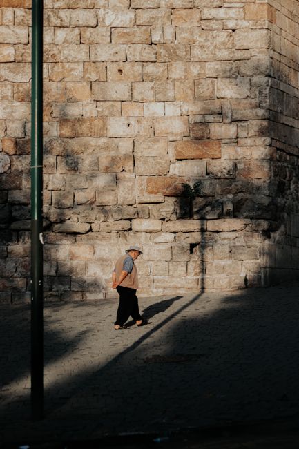A senior adult strolling by a sunlit stone wall in Bursa, Türkiye, capturing a serene urban moment.