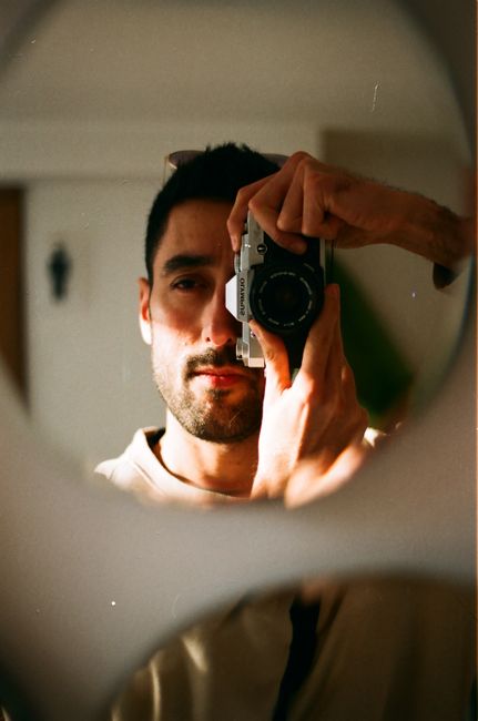Artistic self-portrait of a man using an analog camera for a unique reflection shot.