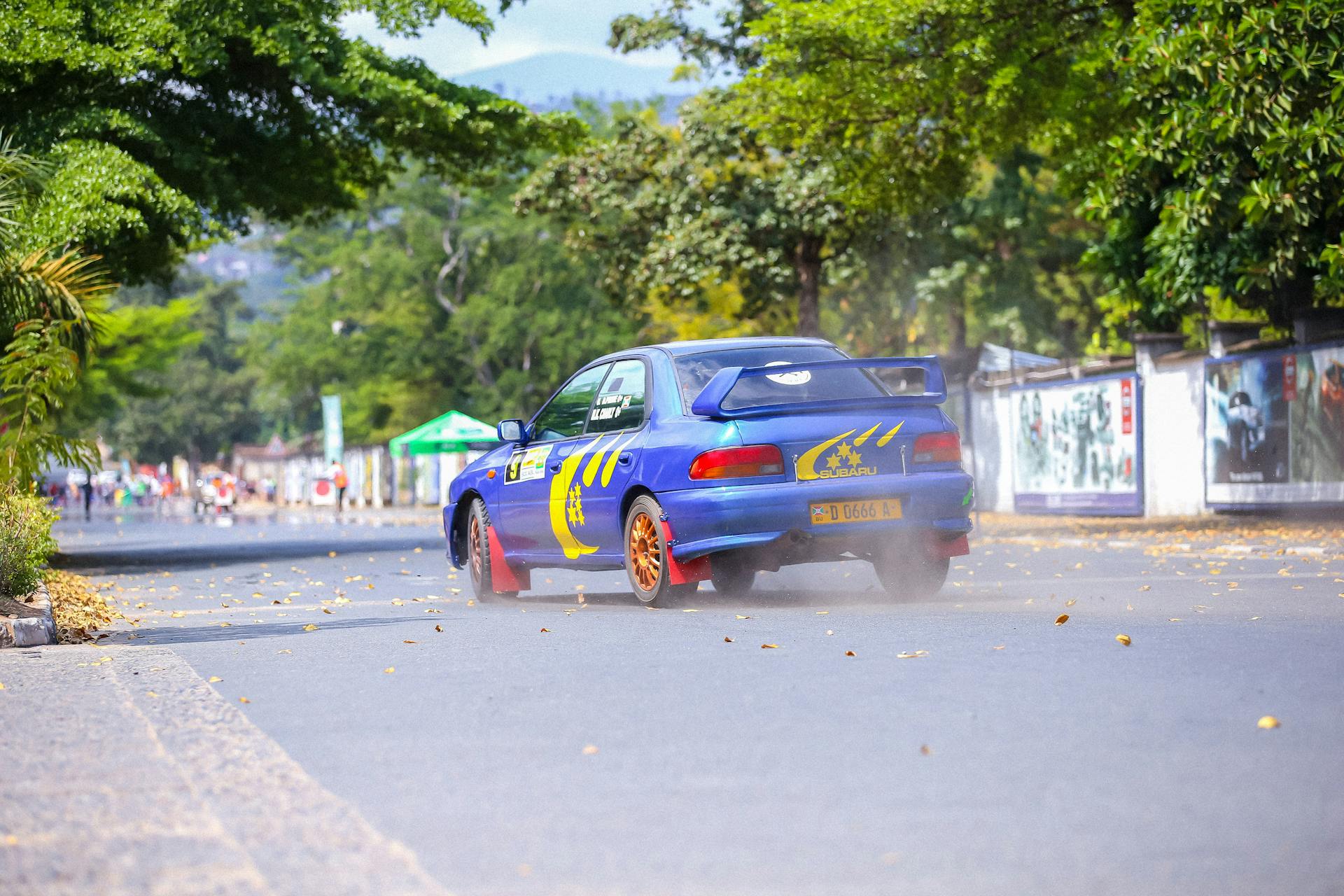 Blue sports car speeding on a tree-lined road during a championship race.