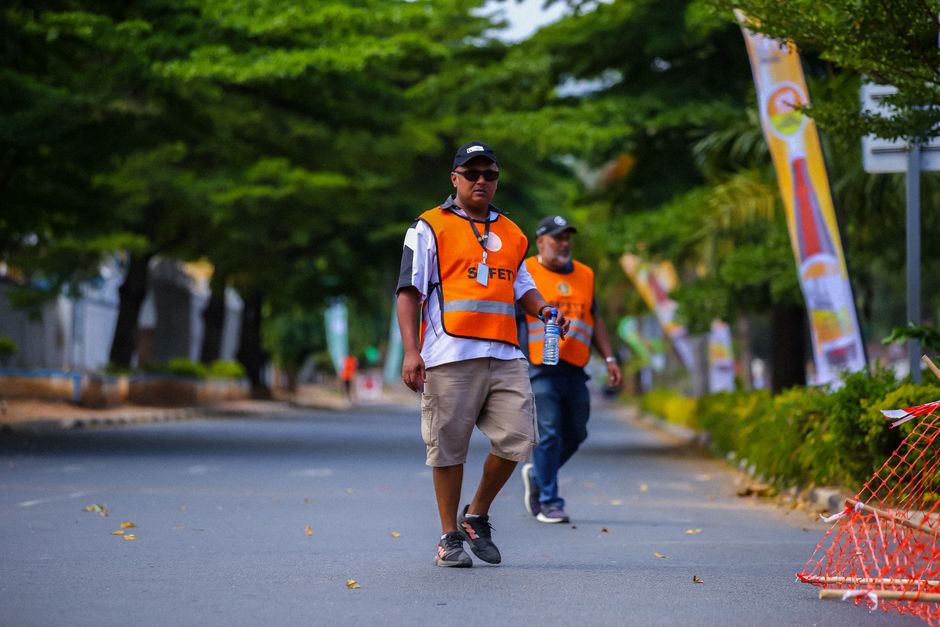 Two safety personnel in reflective vests walking on a tree-lined city street during a sports event.