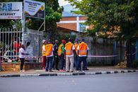 Safety officers wearing orange vests gather in a city street, discussing event security.