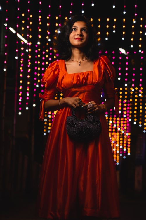 Free Fashionable woman in a red dress standing amid colorful night lights, exuding elegance. Stock Photo