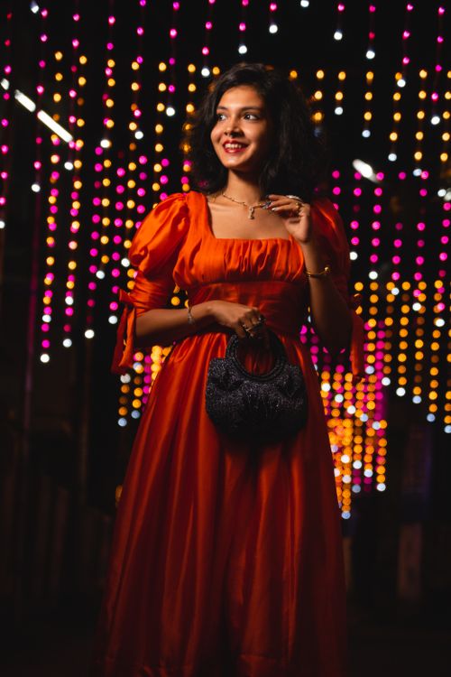Free Elegant woman in a red dress holding a handbag, standing in front of colorful lights. Stock Photo