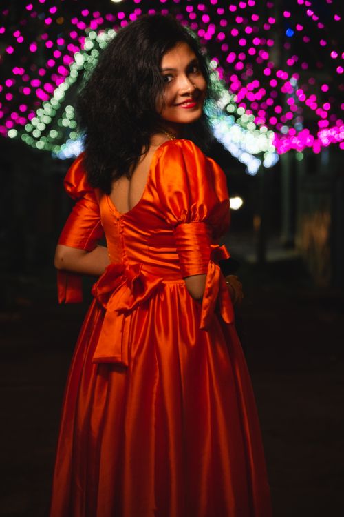 Free Elegant woman in a stunning red dress enjoys a festive night under colorful lights. Stock Photo