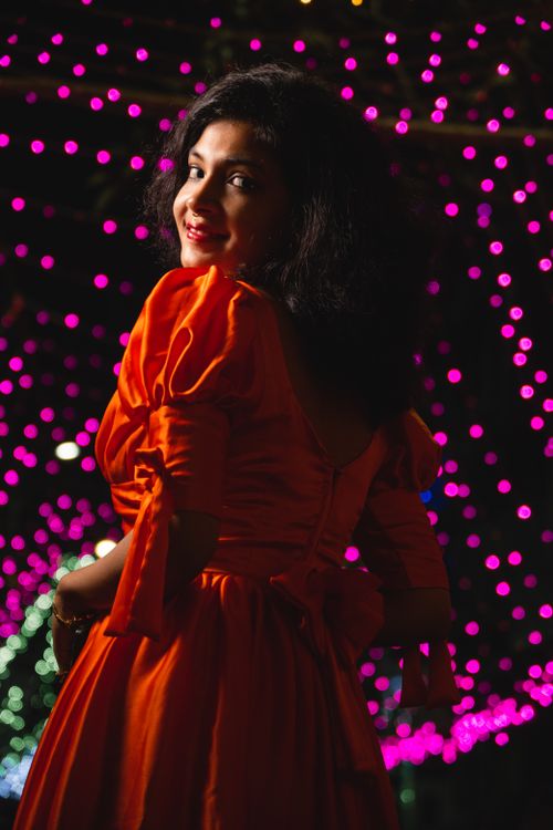 Free Beautiful woman in a red dress posing with festive, colorful lighting backdrop at night. Stock Photo