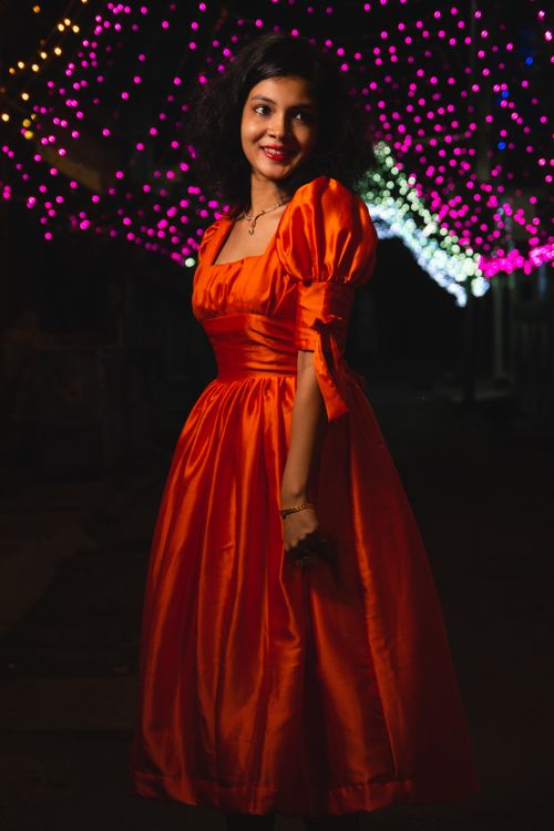 Free A woman in a vibrant red dress poses elegantly under colorful festive lights. Stock Photo